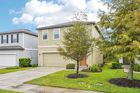 A house with a brown garage door is surrounded by a well-kept lawn and trees.