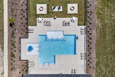 An aerial view of a pool surrounded by a concrete patio and a grassy area.