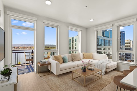 A living room with a white couch and a balcony with a view of the city.