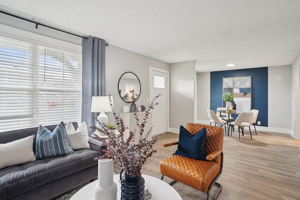 Modern living room with gray sofa, leather chair, round coffee table, and dining area.