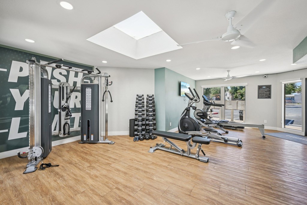 A gym with a variety of equipment including a squat rack, a leg press machine, and a rowing machine.