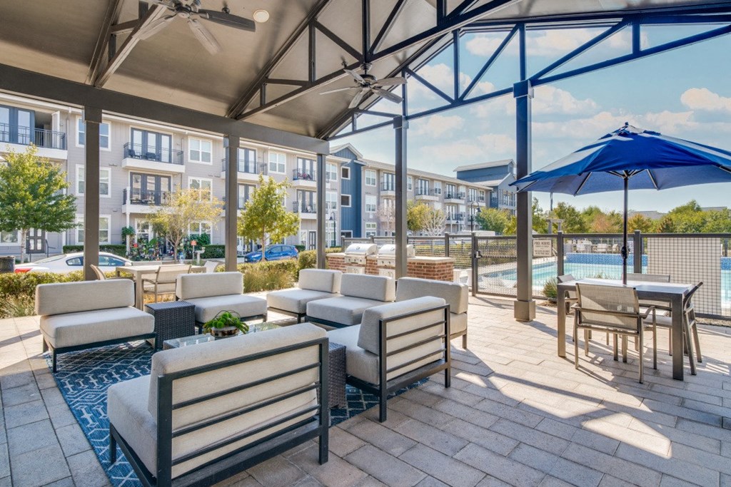 Apartments for Rent in Rowlett, TX - Village of Rowlett - Community Lounge Area Beside Swimming Pool and Grilling Stations with View of Apartment Buildings