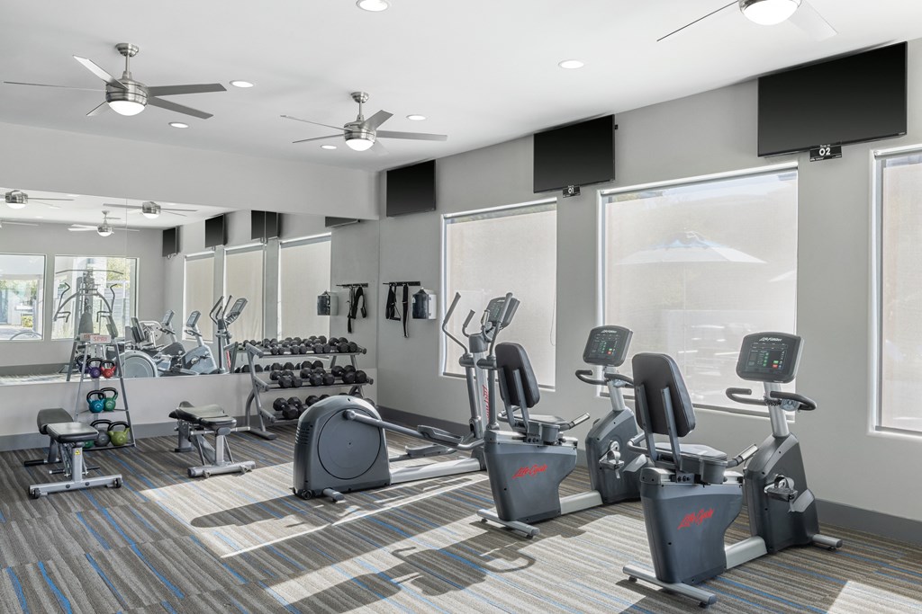 a fitness room with various exercise machines and windows