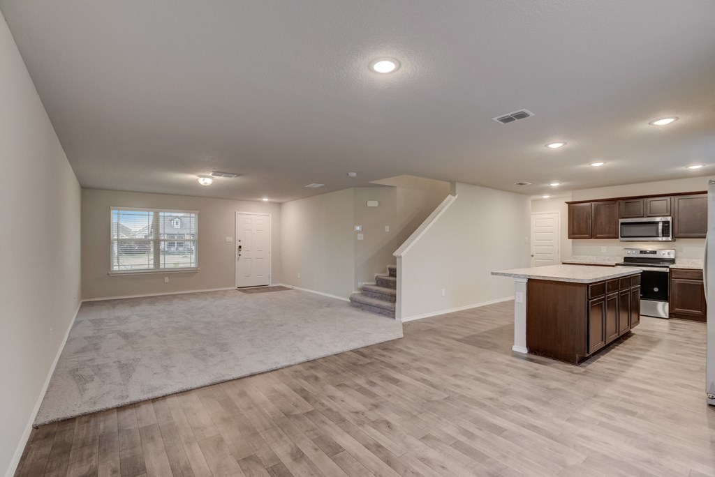 an empty living room with a kitchen and a staircase