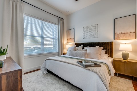 One-Bedroom Apartments in Old East Dallas, TX - 4600 Ross - Bedroom Features A Neatly Made Bed, Soft Neutral Decor, Bedside Lamps, And Framed Wall Art.
