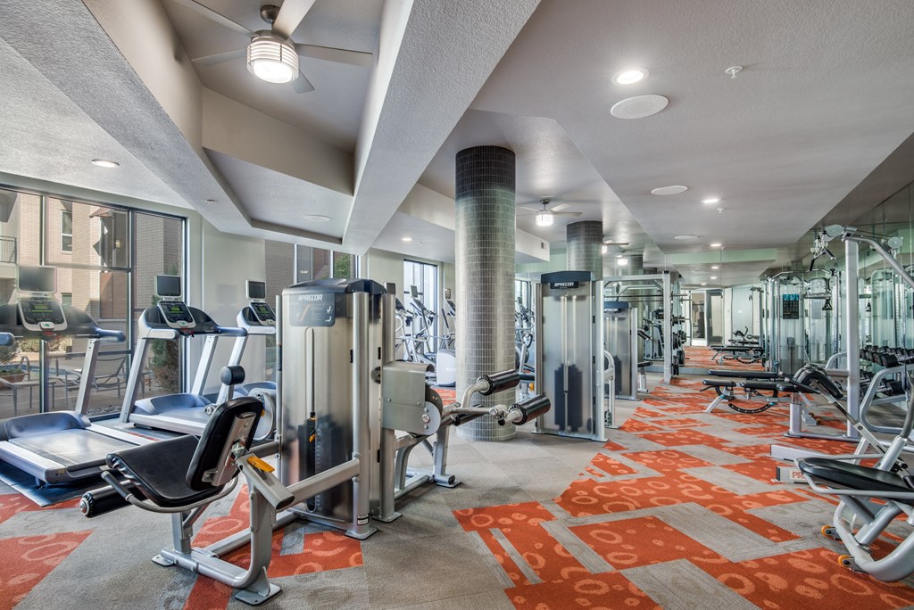 a fitness center with cardio equipment and weights in a building with windows