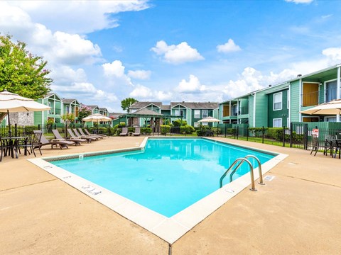 A swimming pool surrounded by lounge chairs and umbrellas in a residential area.