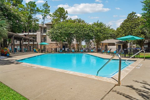 A large swimming pool surrounded by trees and a building in the background.