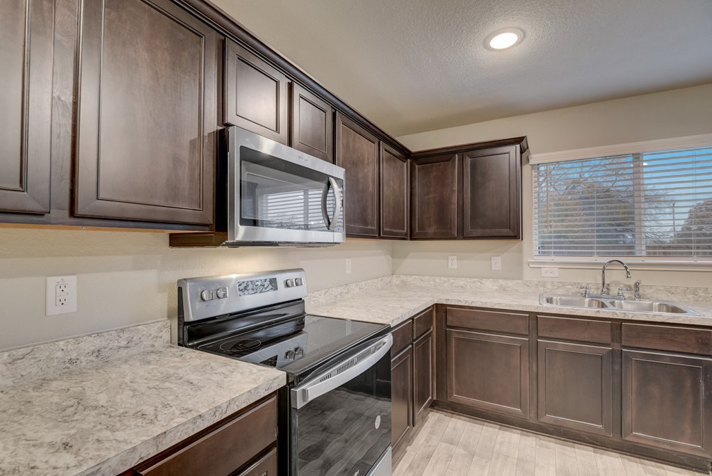 a kitchen with dark wood cabinets and granite counter tops and a stove and microwave