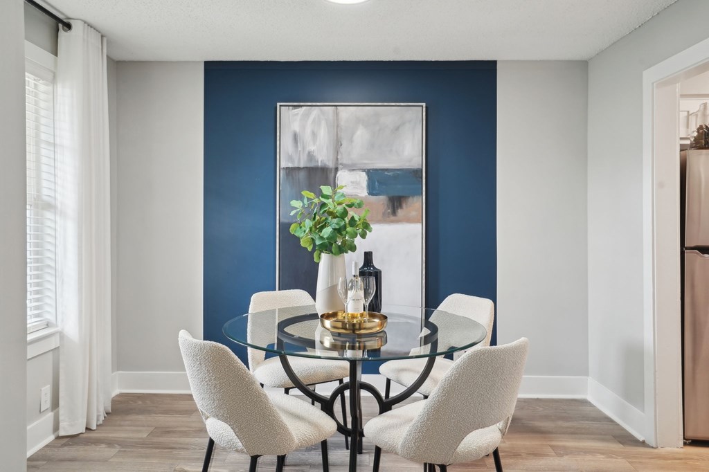 Modern dining room with glass table, four chairs, and blue accent wall.