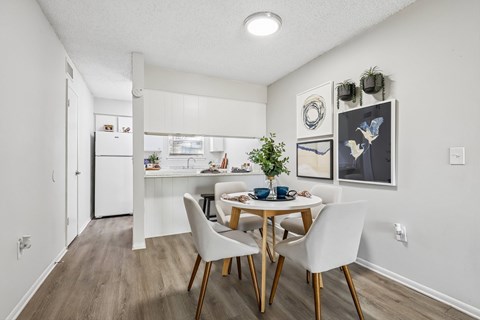 A dining room with a table set for two and a kitchen in the background.