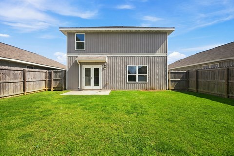 A house with a grey exterior and a white door is surrounded by a green lawn.