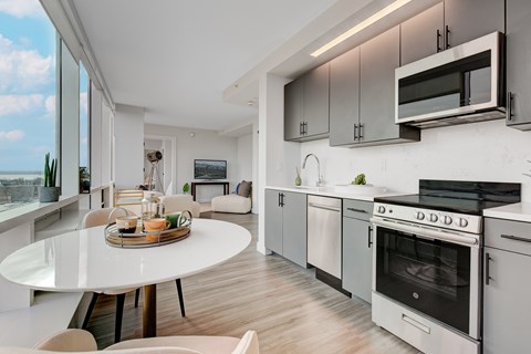 A modern kitchen with a white table and chairs, a microwave above the stove, and a view of the ocean through the window.