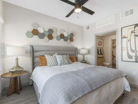 A bedroom with a bed, a ceiling fan, and a wall art.