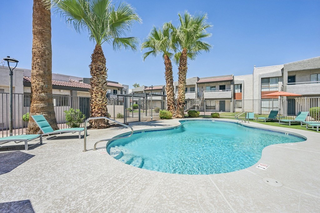 A pool surrounded by palm trees and lounge chairs.