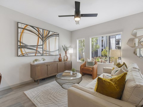 A living room with a large abstract painting on the wall, a white sofa, and a glass coffee table.