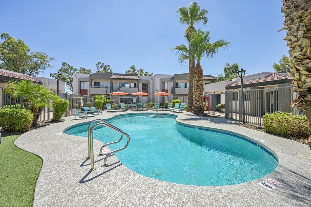 A large swimming pool surrounded by a concrete patio and a metal fence.