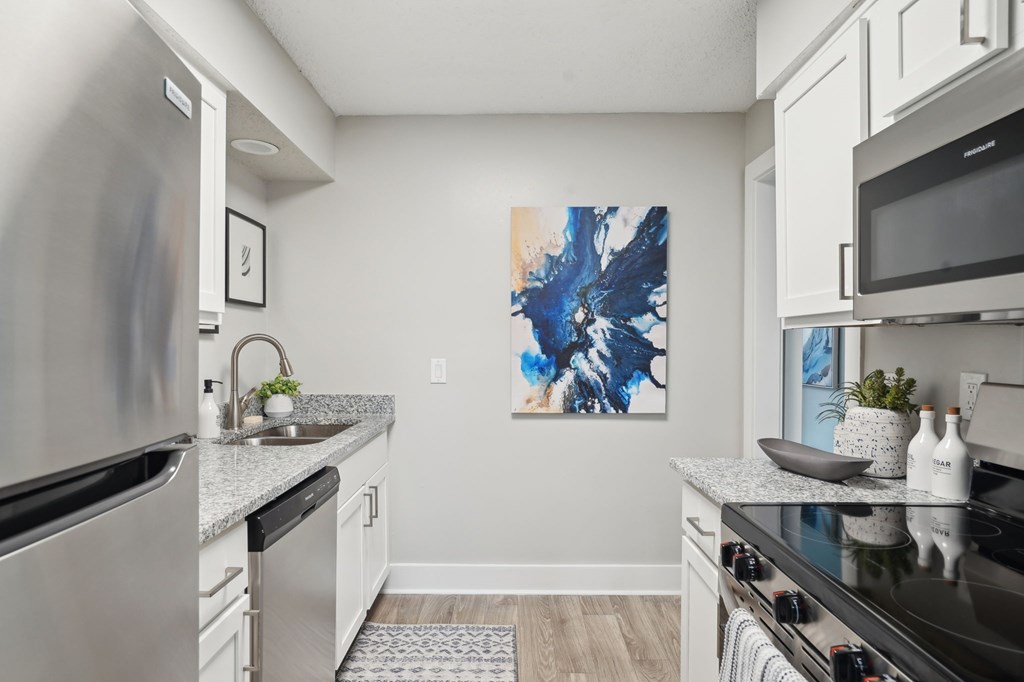 Modern kitchen with stainless steel appliances, white cabinets, granite countertops, and abstract art.