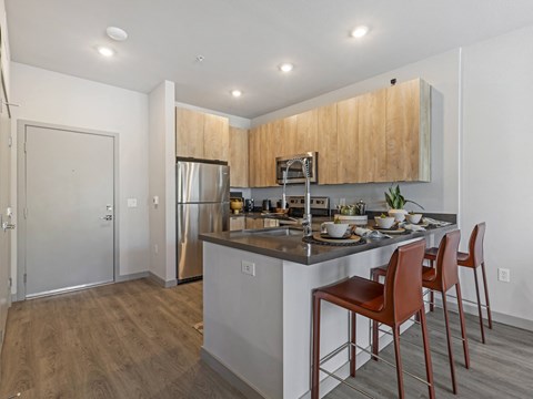 A kitchen with a refrigerator, sink, and bar stools.