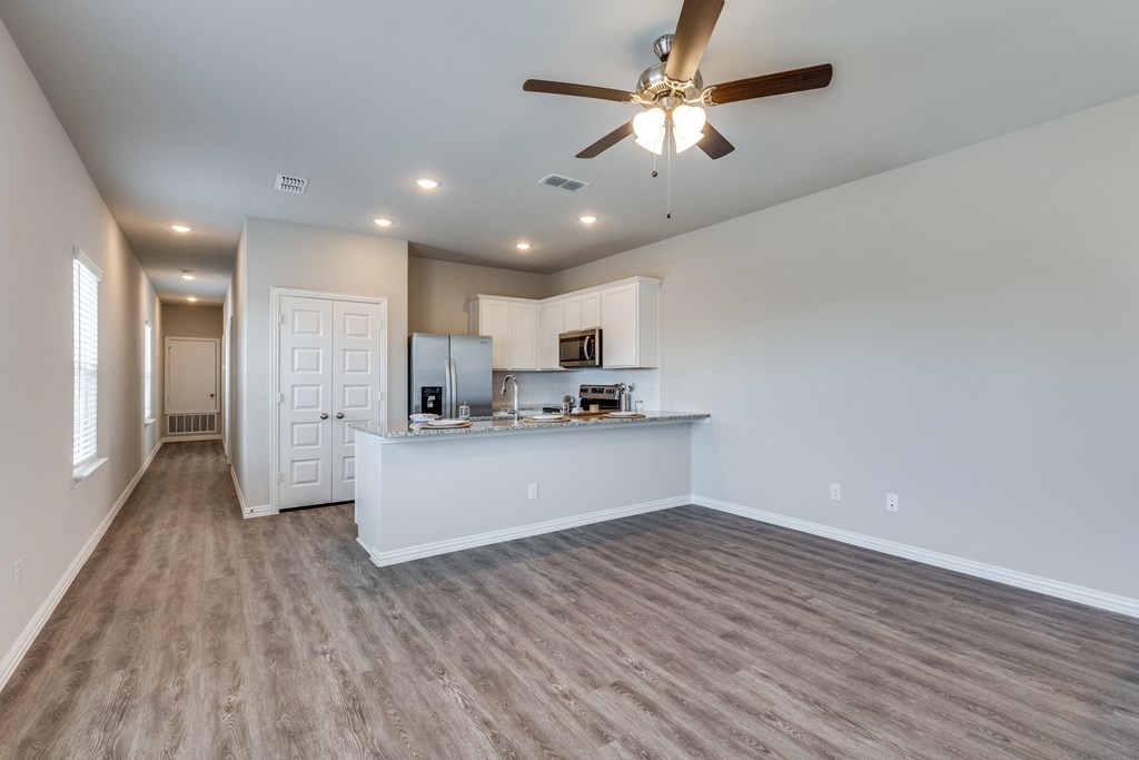 an empty living room with a kitchen and a ceiling fan