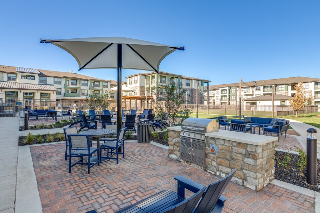 a patio with a grill and tables with chairs and umbrellas