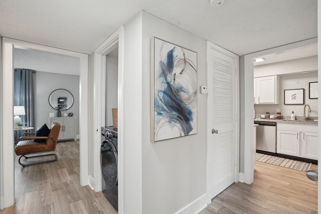 Apartment hallway with laundry area, abstract art, and views into the living room and kitchen.