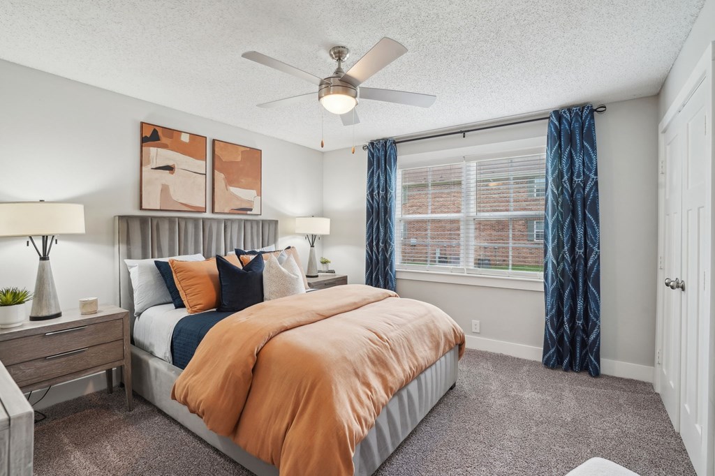 Modern bedroom with gray headboard, orange bedding, blue curtains, and abstract art.