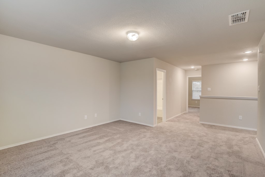 an empty living room with carpet and a door to a kitchen