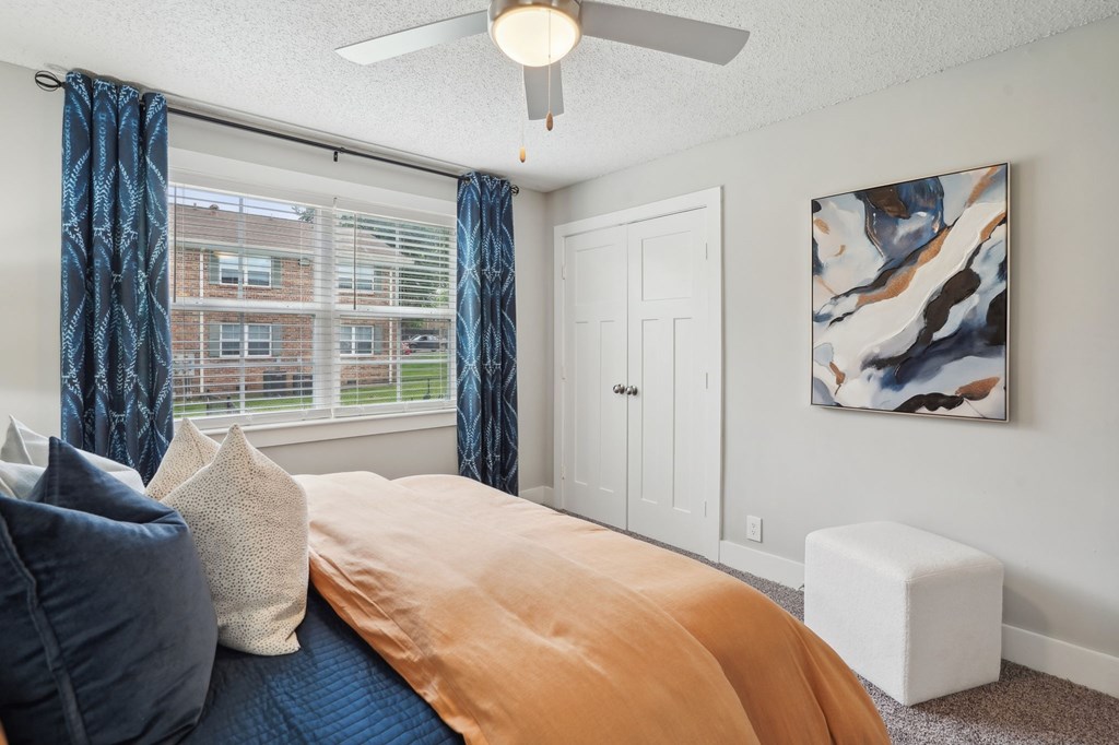 Bedroom interior with blue and orange bedding, window with blue curtains, and abstract art.