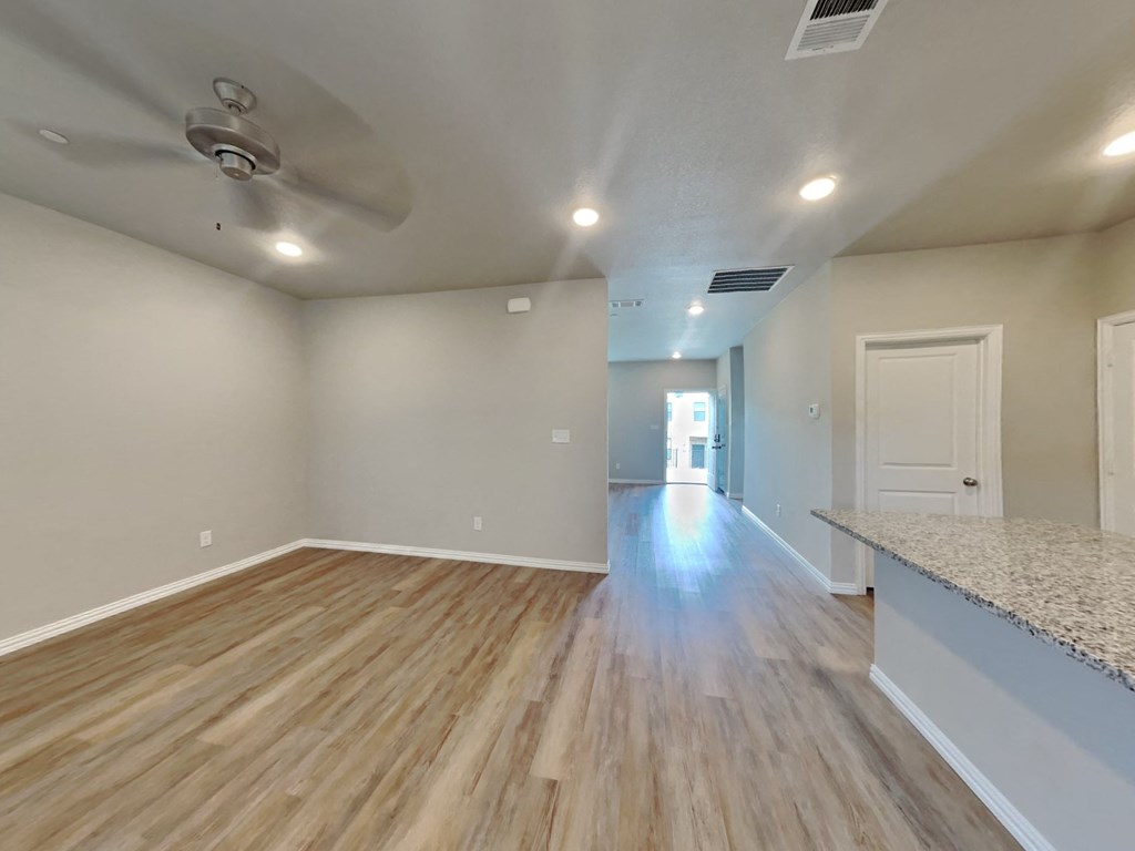 an empty living room and kitchen with hardwood flooring and a ceiling fan