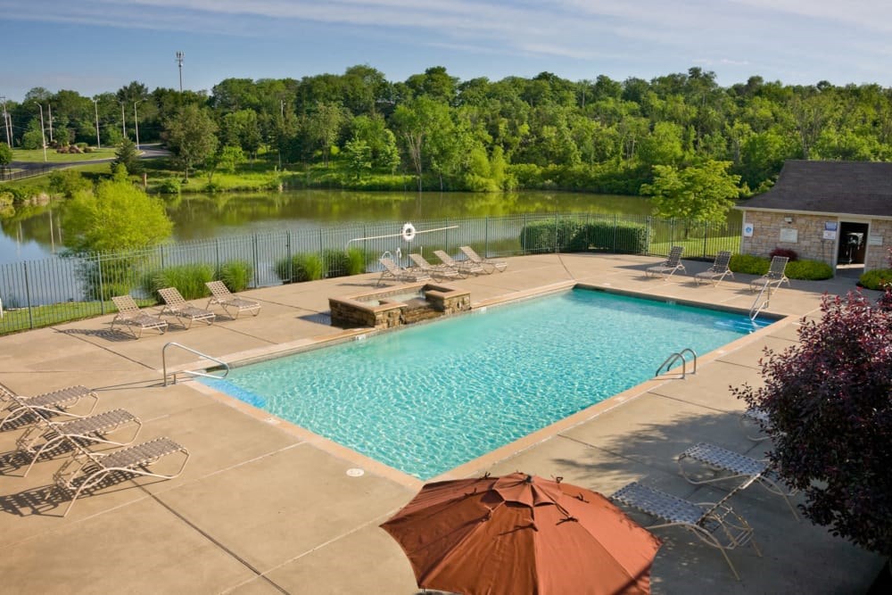 a swimming pool with chaise lounge chairs and a fire pit with a lake in the background