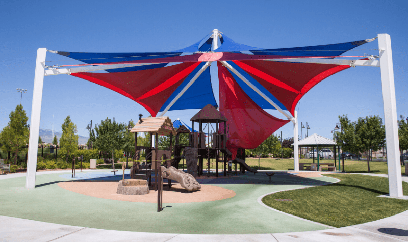 a large red and blue canopy over a playground at a park