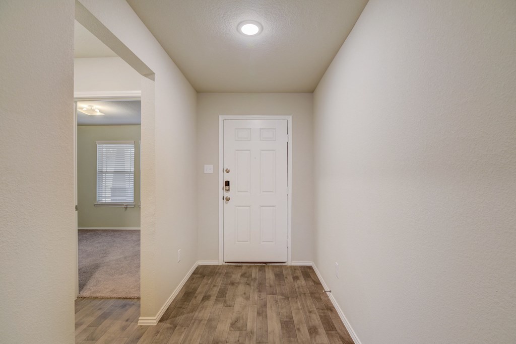 an empty living room with a white door and a hallway to a bedroom