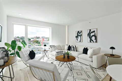 A living room with white furniture and a large window overlooking a cityscape.