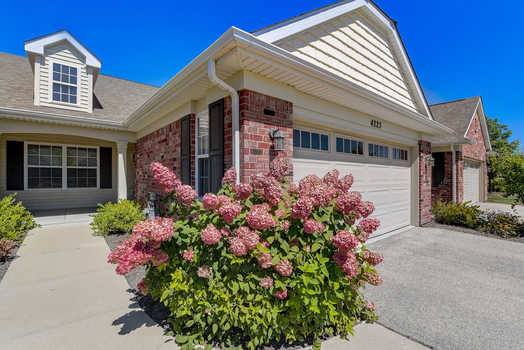 the front of a house with a garage door and pink flowers