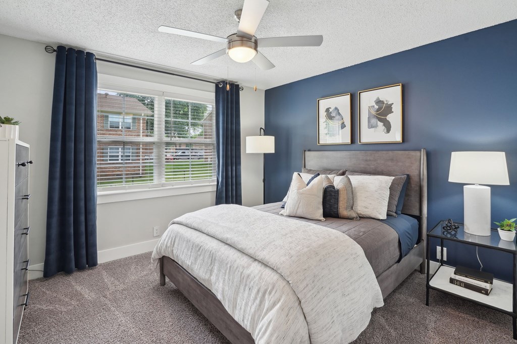 Bedroom with blue accent wall, grey bed, and window view.
