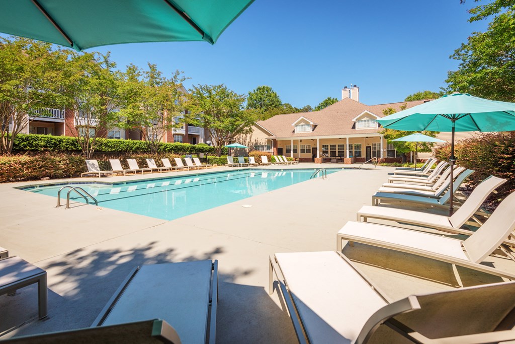 a swimming pool with chairs and umbrellas and a house in the background