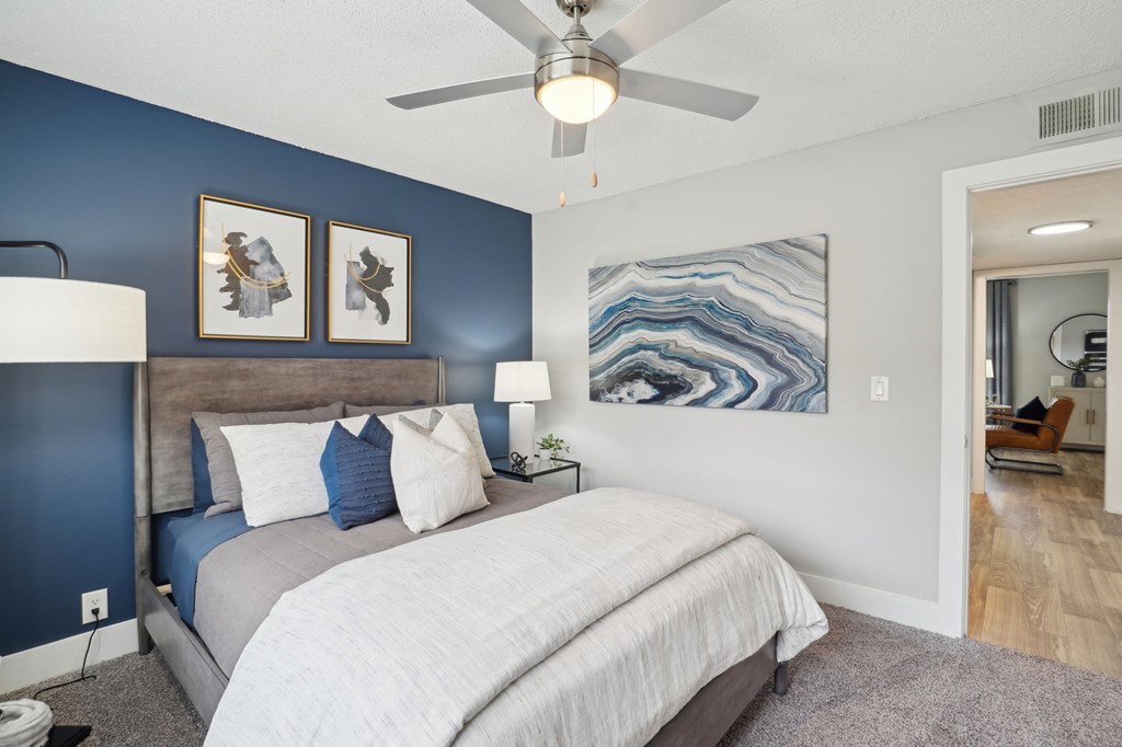 Modern bedroom with blue accent wall, gray bed, and abstract art.