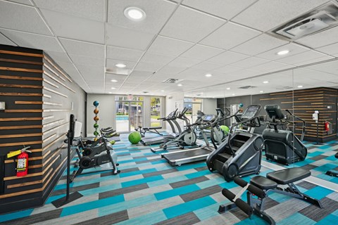 Apartment complex fitness center with treadmills, stair climbers, exercise bikes, and colorful flooring.