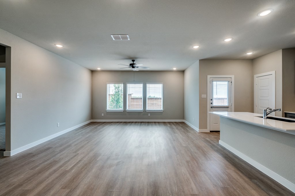 an empty living room with a kitchen and a ceiling fan