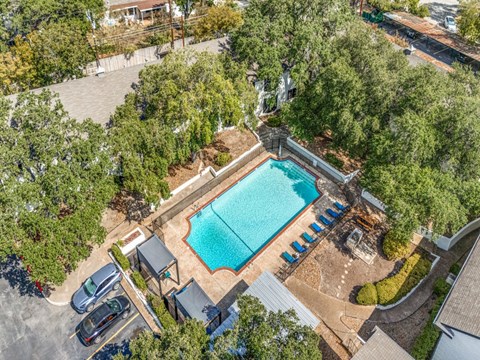 An aerial view of a swimming pool surrounded by trees and a parking lot.