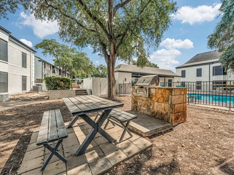 3-Bedroom Apartments in Alamo Heights, TX - The Landmark at Alamo Heights - Outdoor Grill with Picnic Table and Benches, Built-In Stainless Steel Grill on Stone Bricks, and Metal Fence