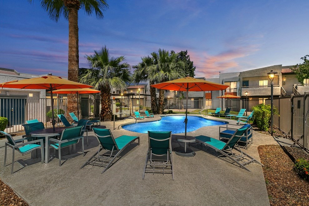 Pet-Friendly Apartments in Glendale, AZ - Ardella on 67th - Gated Shimmering Swimming Pool with Lounge Seats, Tables, Chairs, Umbrellas, and Palm Trees.