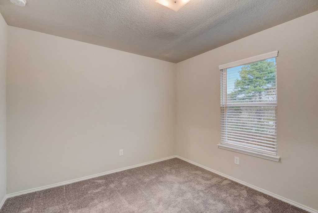 an empty bedroom with a window and carpeting