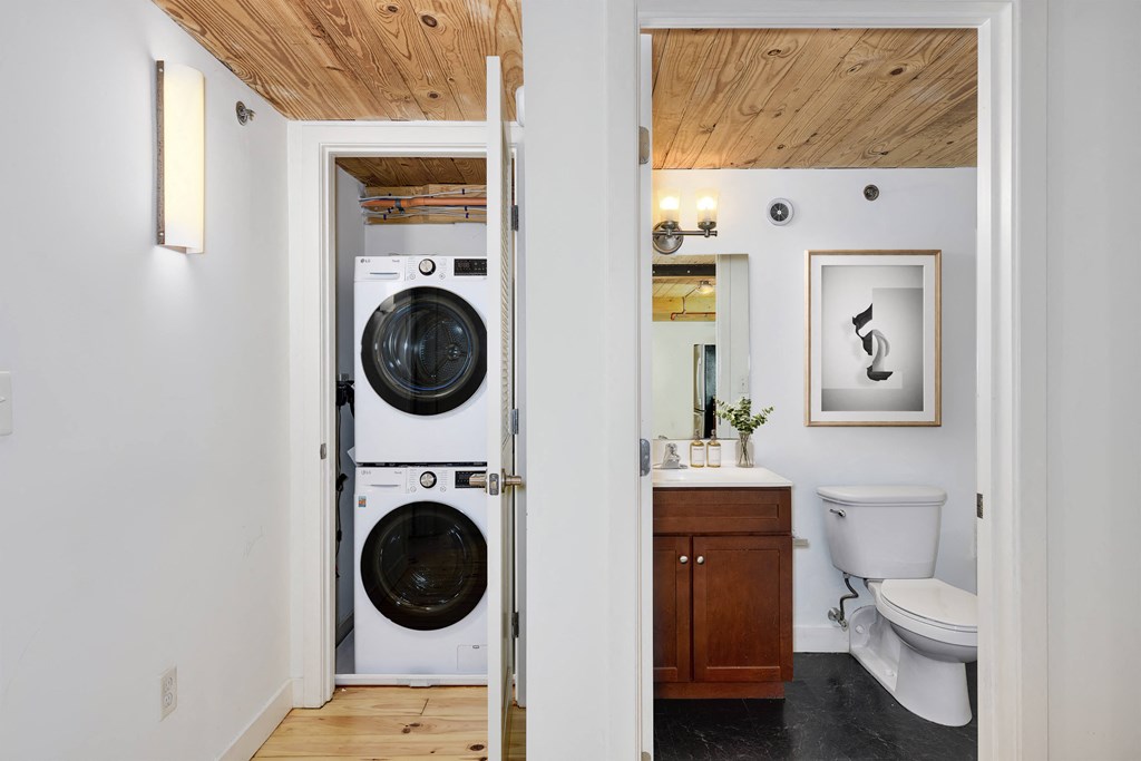 Modern bathroom with stacked washer and dryer, wood ceiling, vanity, and toilet.