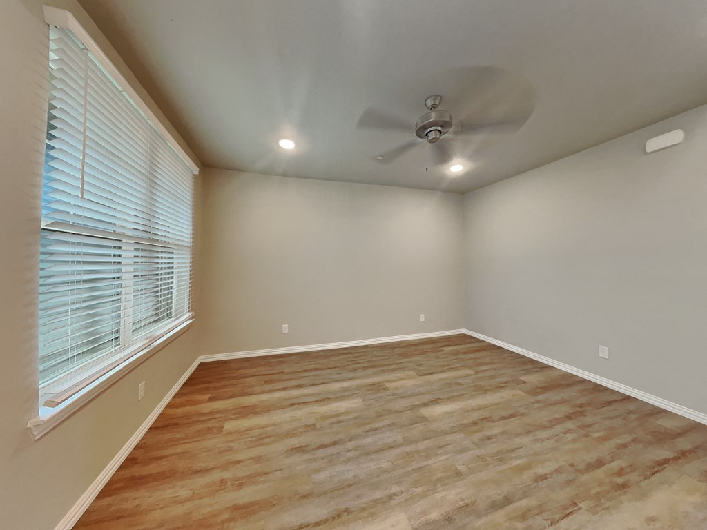 an empty living room with a large window and a ceiling fan