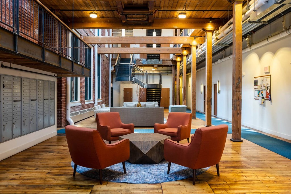 Modern lounge area with orange armchairs, geometric coffee table, and exposed wooden beams in a renovated industrial building.