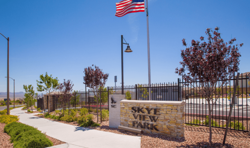 a stone sign with an flag and a sidewalk in front of a fence