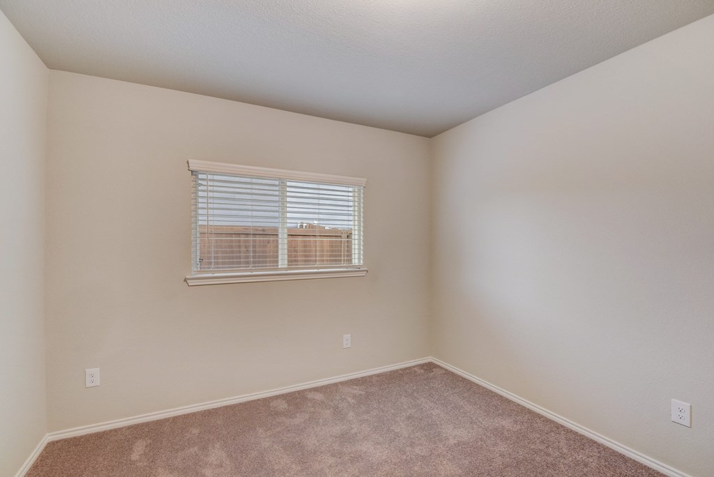 an empty bedroom with a window and carpeting