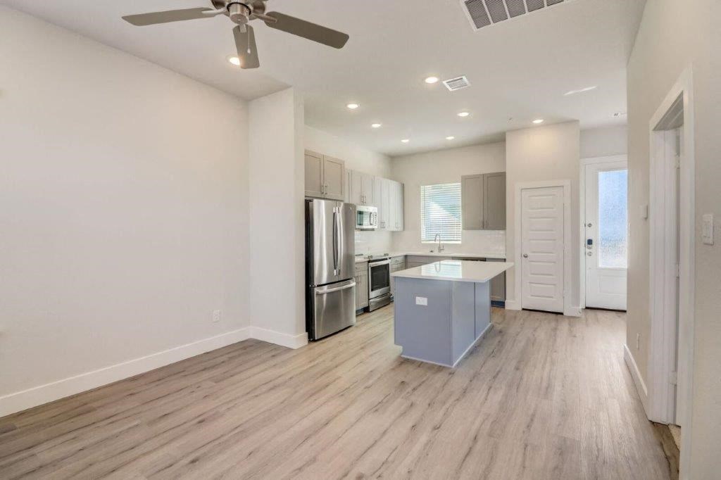 an empty living room with a kitchen and a ceiling fan